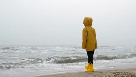 Child in a yellow rain jacket. A child in a storm runs along the beach Odessa Stock Footage 103352289