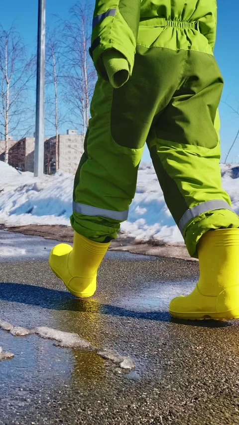 Child in yellow rubber boots walking in thawing snow on wet sidewalk, vertical Stock Footage 265014869