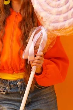 Childlike fun with oversized candy stick and bright orange backdrop Stock Photos