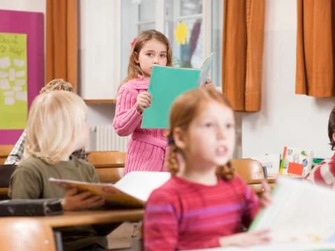 Children (4-7) in classroom, focus on girl reading book in background Stock Photos