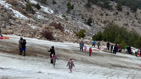 Children from all sides going down on sleighs, muslim woman walking up with Stock Footage 231140776