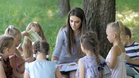 Children and education, young woman at work as educator reading book to boys and Stock Footage