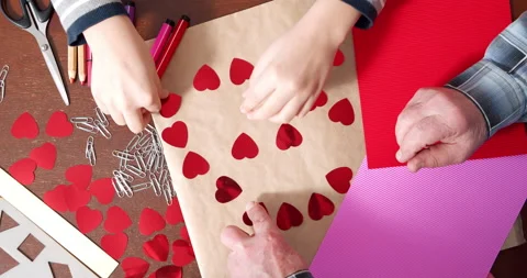 Children and elderly hands making handmade cards by laying out hearts on paper Stock Footage 147030953