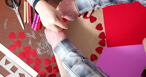 Children and elderly hands making handmade cards by laying out hearts on paper Stock Footage 147034237