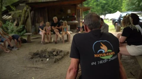 Children and instructors sitting in circle around fire pit at outdoor camp Stock Footage 330953898