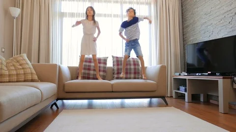The children are having fun. A boy and a girl are jumping on the couch.  Stock Footage 77408022