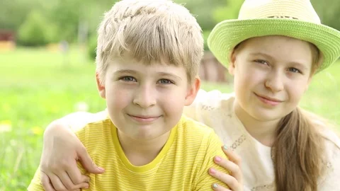 The children are looking at the camera. The smiling sister hugs her brother.  Stock Footage 76497444
