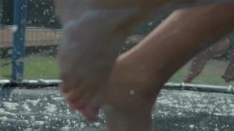 Children bouncing on trampoline playing in summer with water close up Stock Footage 135796741