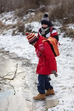 Children in bright winter clothes explore a snowy area near a frozen pond. .. Foto stock