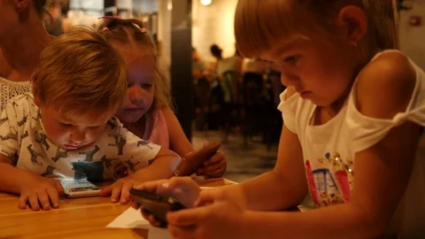 Children at cafe table enjoy watch mobile phone cartoons type slide game app Stock Footage 78217474