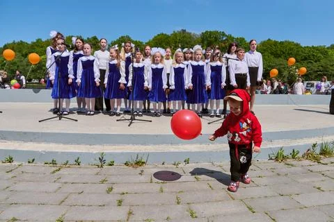 Children choir performing outdoors while child plays with red ball Stock Photos