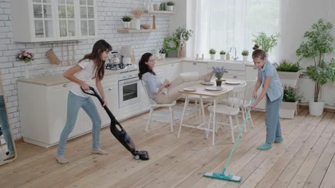 Children clean up while mom drinks coffee and enjoys free time. Little girls Stock Footage 148624696