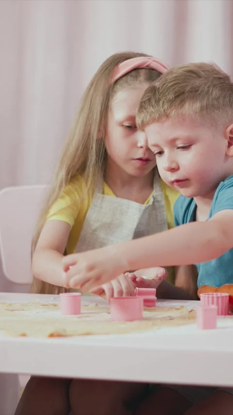 Children collaboratively bake using pink cookie cutters and dough at table with Stock Footage 345982118