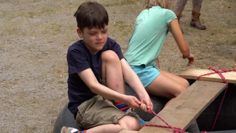 Children constructing wooden raft by tying ropes to planks during outdoor camp Stock Footage 330877969