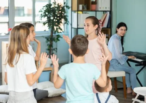 Children dancing in circle while teacher plays music on synthesizer Stock Photos