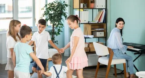 Children dancing in circle while teacher plays music on synthesizer Stock Photos