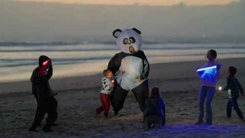 Children dancing with inflatable panda mascot on beach at sunset Stock Footage 330499848