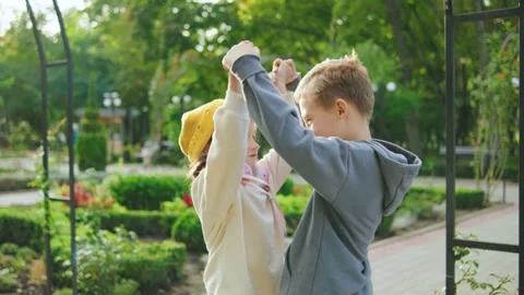 Children dancing joyfully in a garden during a sunny afternoon, surrounded by Stock Footage 305418652