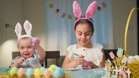 Children decorate Easter eggs sitting at the table in the living room. Stock Footage 233626146