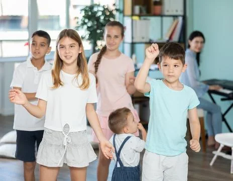 Children of different ages doing round dance together with young teacher Stock Photos