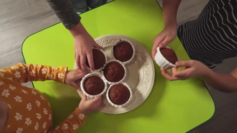 Children of different ages take muffins from the dish on the table, top view. Video stock 169382269