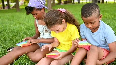 Children of different races sit on the grass and play with an anti-stress toy Stock-Footage 169921148