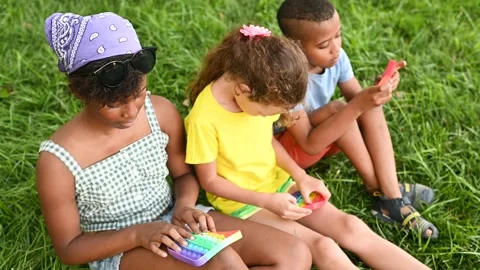 Children of different races sit on the grass and play with an anti-stress toy Stock-Footage 169921223