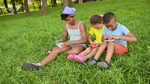 Children of different races sit on the grass and play with an anti-stress toy Stock Footage 171218652