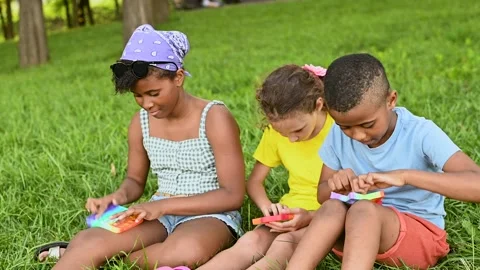 Children of different races sit on the grass and play with an anti-stress toy Stock-Footage 172500929