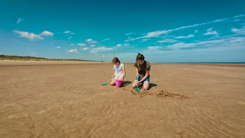 Children digging sand on wide beach with bucket and spade, enjoying sunny day. Stock Footage 329068537