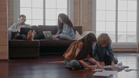 Children draw on the floor while their parents sit on the couch working Видео 165411581