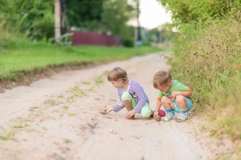 Children draw with a stone on the sand while squatting on a sandy village roa Foto stock