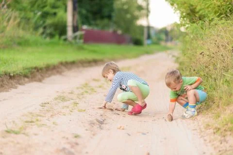 Children draw with a stone on the sand while squatting on a sandy village roa Stock-Fotos