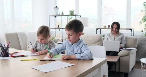 Children drawing on paper while mother is working on laptop at home Video stock 156542873