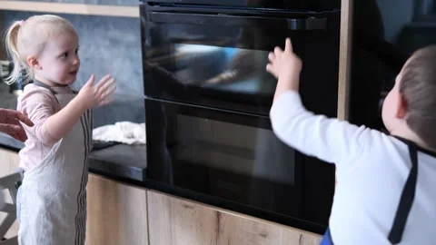 Children eagerly watching a pastry bake through the oven door, filled with Stock Footage 289519142
