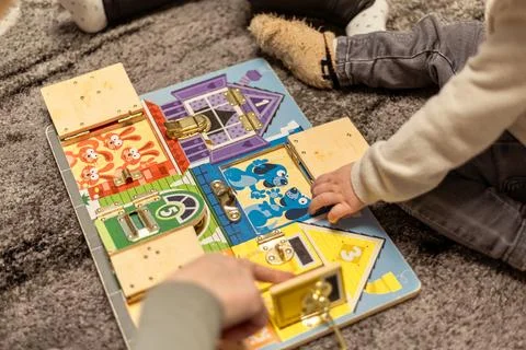 Children engage in playful learning with an interactive lock board on a cozy rug Stock Photos