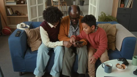 Children Explaining Mobile App to Senior Black Man Sitting on Sofa Stock Footage 322526025