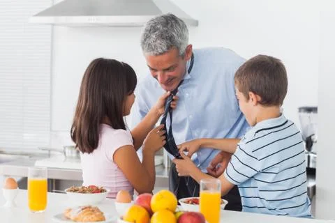 Children fixing their fathers tie in the kitchen Stock Photos