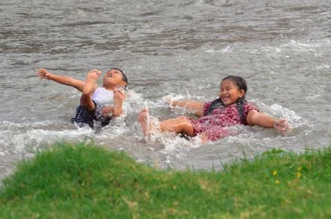 Children float side-by-side laughing in river stream Stock Photos