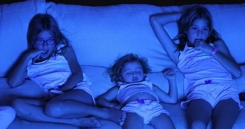 Children in front TV screen watching movie seated on couch at night in the da Stock Footage 116714657