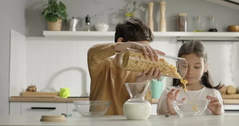 Children have corn flakes at breakfast. Little boy pours cereal into girl's bowl Stock Footage 265287378