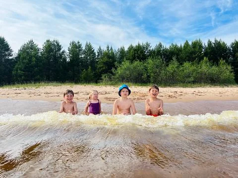 Children having fun catching waves in Ladoga lake. Summer vacations on beach Fotos de archivo