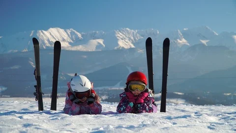 Children in helmets and goggles lying on snowy terrain with skis near on Vidéo 105701649