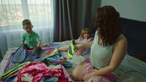 Children help mom put clothes in a suitcase for vacation at sea. Stock Footage 248763158