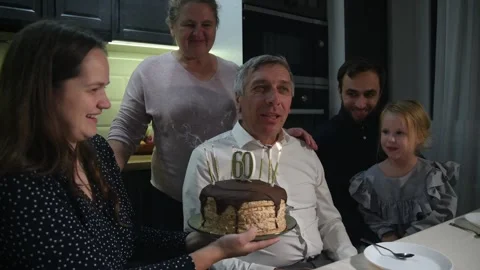 Children hold a birthday cake while their father blows out the candles. Stockbeeldmateriaal 340063249