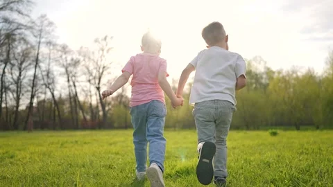 Children hold hands while running on field. Girl and boy enjoy outdoor activity Vídeos de archivo 319248927