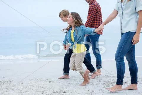 Children holding hands while walking with parents at sea shore Stock Photos
