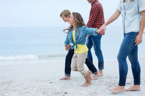 Children holding hands while walking with parents at sea shore 스톡 사진