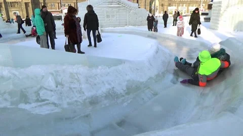 CHILDREN IN ICE TOWN MOVE DOWN FROM ICE SLIDE. CHELYABINSK, RUSSIA. 5 Stock Footage 60364702