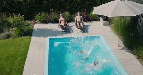 Children jump into the pool, slow motion video. Adults rest on sun loungers Stock Footage 250022077